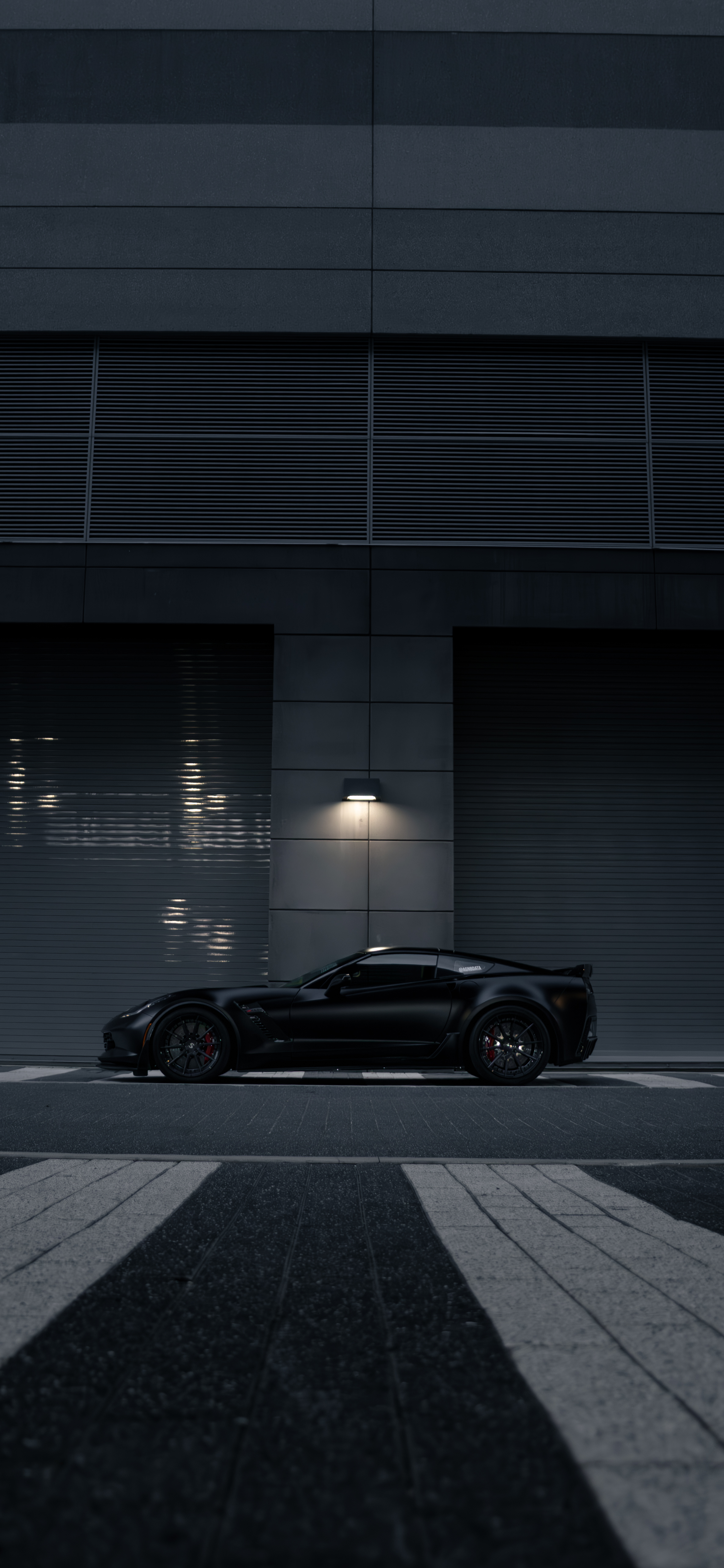Side profile of the black Chevrolet Corvette C7 Z06 parked outside an industrial building.